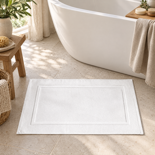 Bath Mat Jarmila in white on a stone floor beside a bathtub