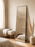 Mirror Peter leaning against a warm bedroom wall beside a bouclé bench and pampas grass