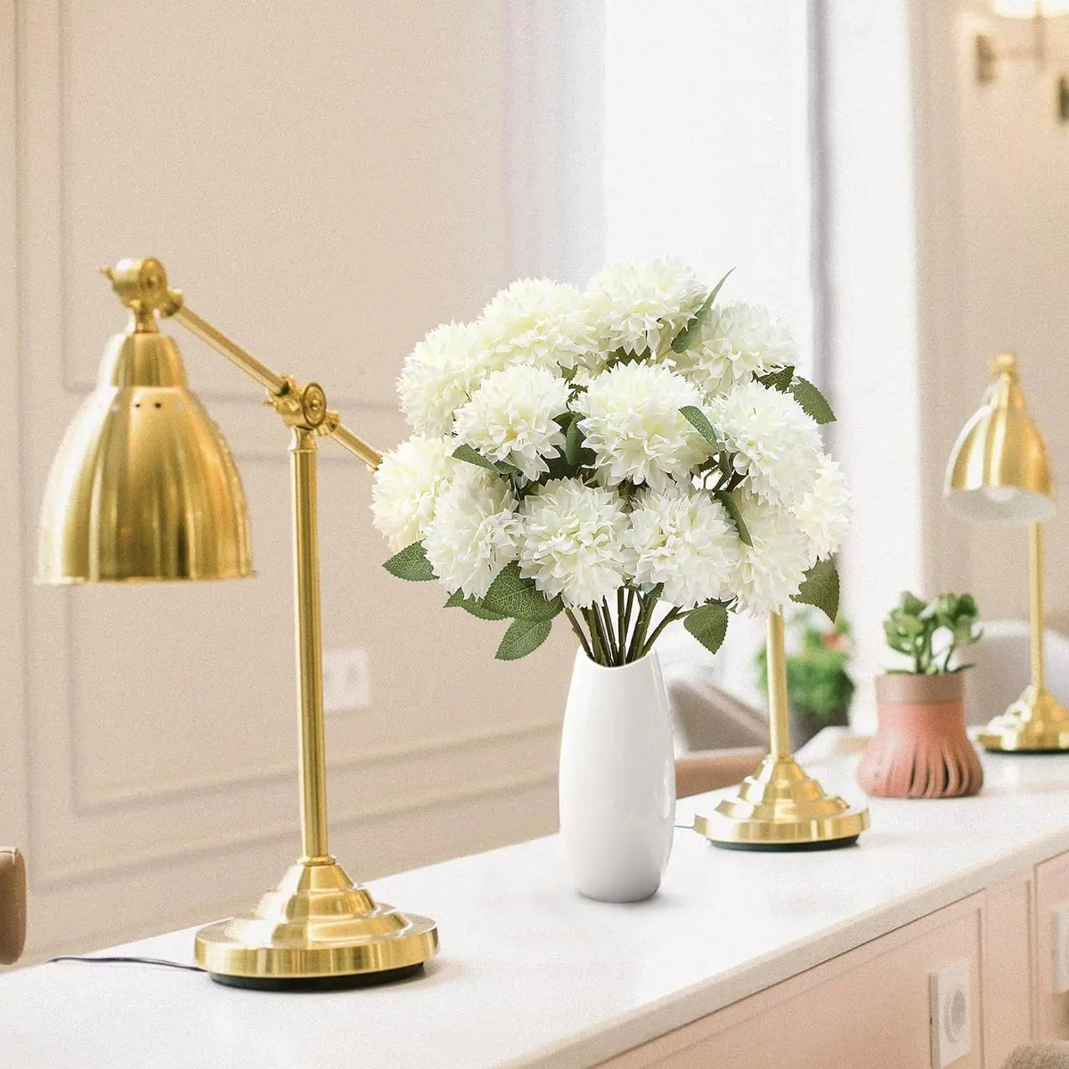 White chrysanthemum stems in a white vase on a sideboard with brass lamps