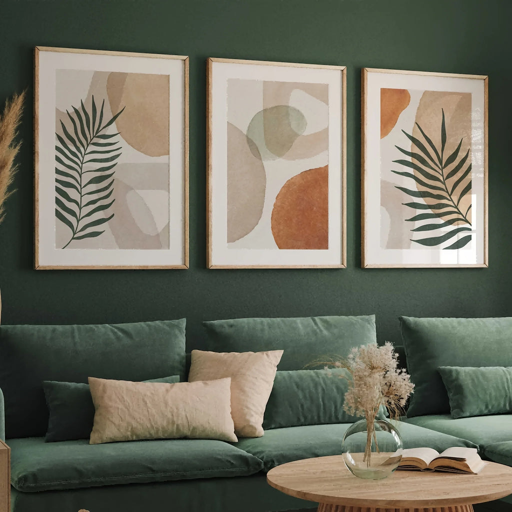 Three leaf and terracotta art prints above a green sofa, shown framed for illustration