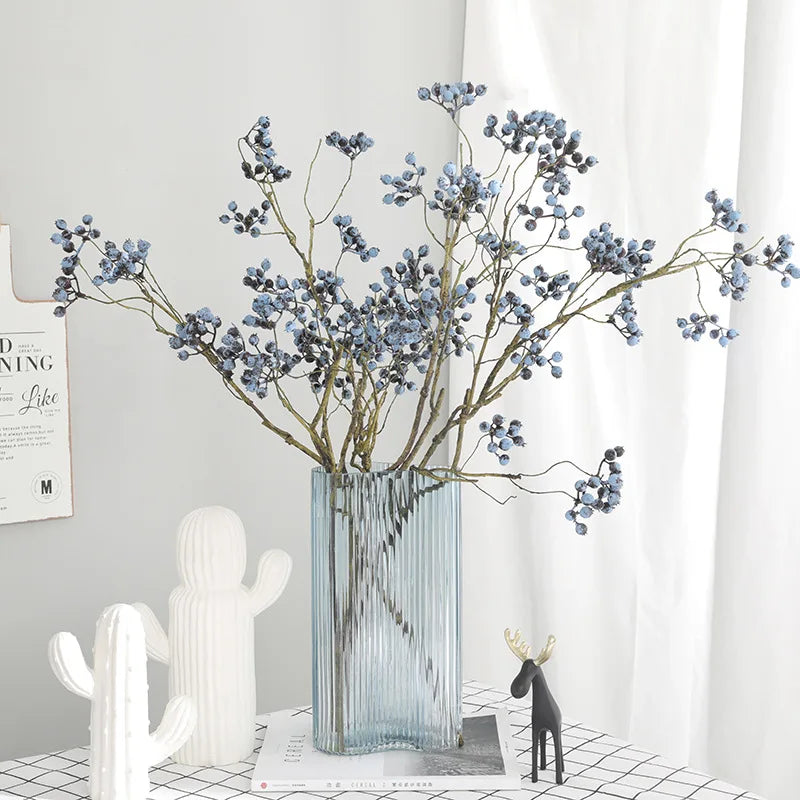 Dusty blue faux berry branches in a ribbed glass vase on a shelf
