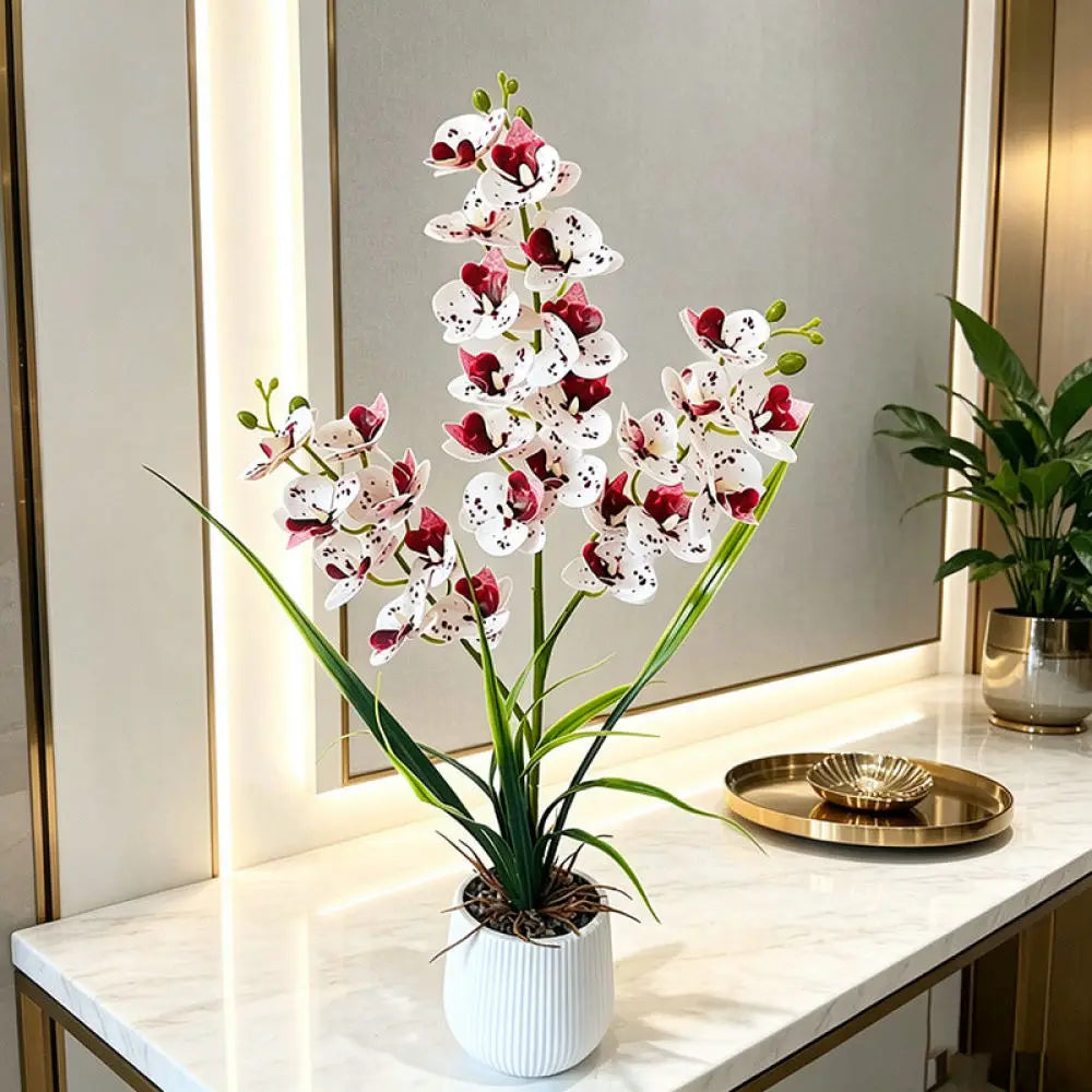 Artificial white orchid with burgundy spots in a white pot on a marble console