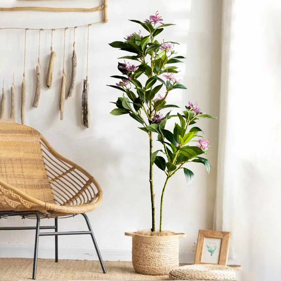 Faux flowering stem Denisa with pink blossoms in a woven basket by a rattan chair