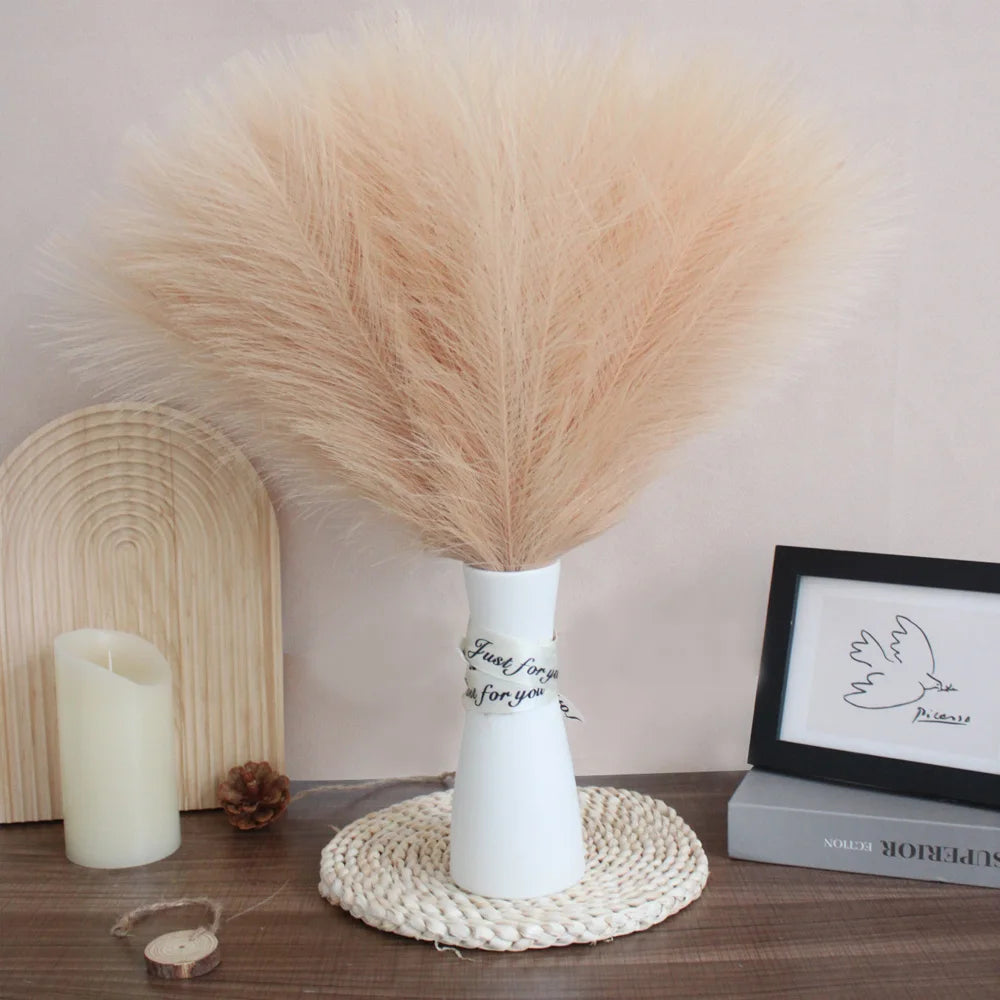 Beige faux pampas grass stems in a white vase on a wooden shelf