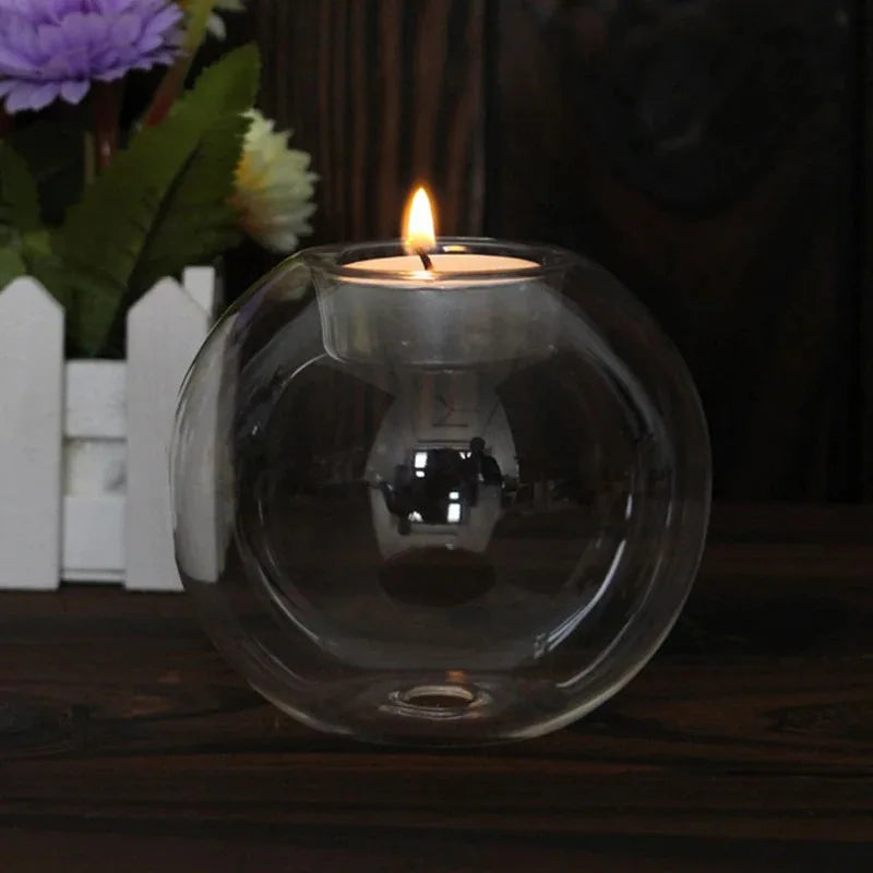 Clear glass tealight holder with a lit tealight in front of purple flowers