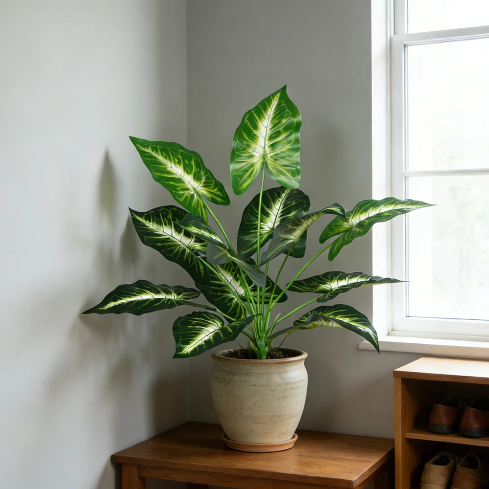 White-veined faux leaf plant in a stone pot beside a window