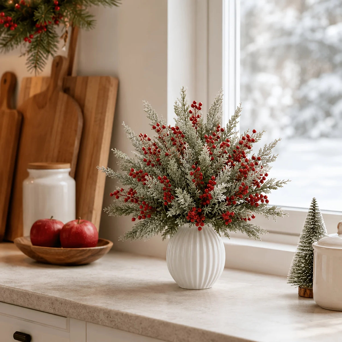 Snowy pine and red berry stems in a vase on a kitchen counter