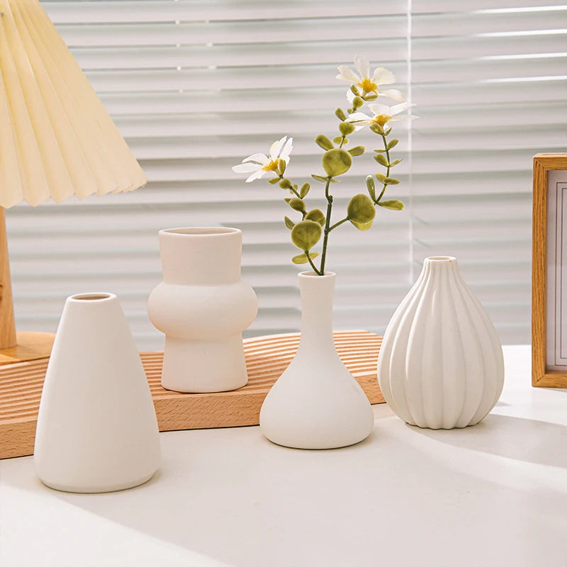 Matte white ceramic bud vases with a white flower and eucalyptus on a wooden tray