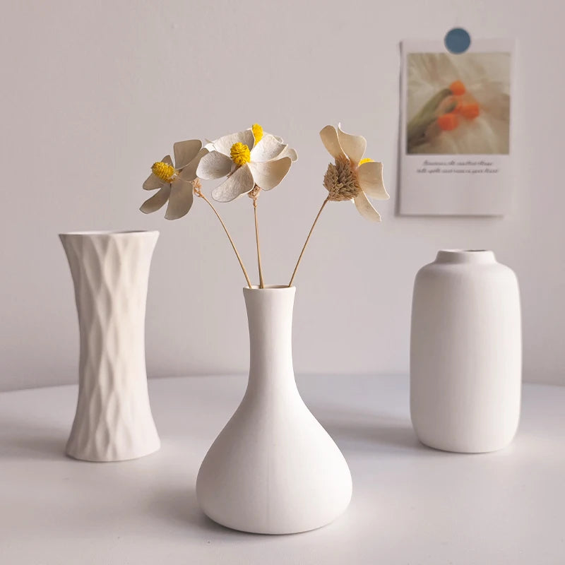 Three matte white ceramic vases with dried flowers on a white table