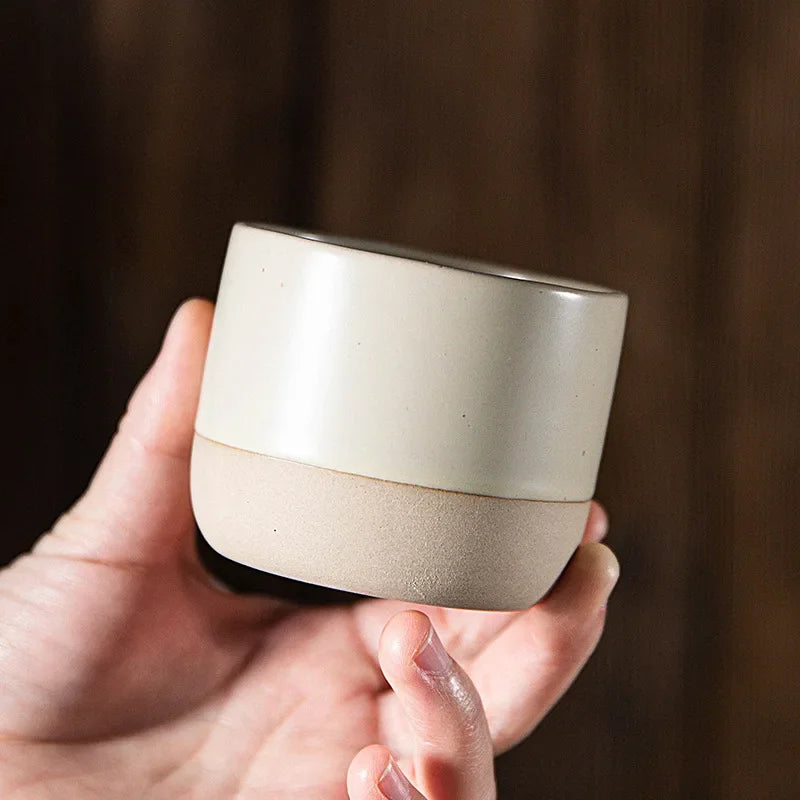 Hand holding a cream ceramic cup with an unglazed natural base