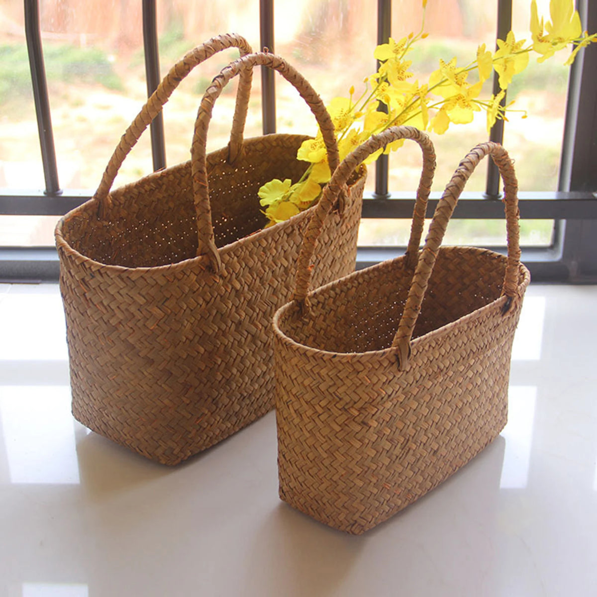 Two woven seagrass baskets with handles by a window, with yellow flowers
