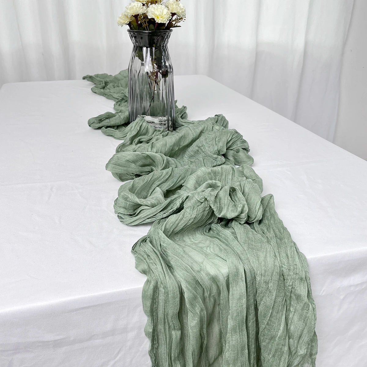 Sage gauze table runner on a white dining table with a vase
