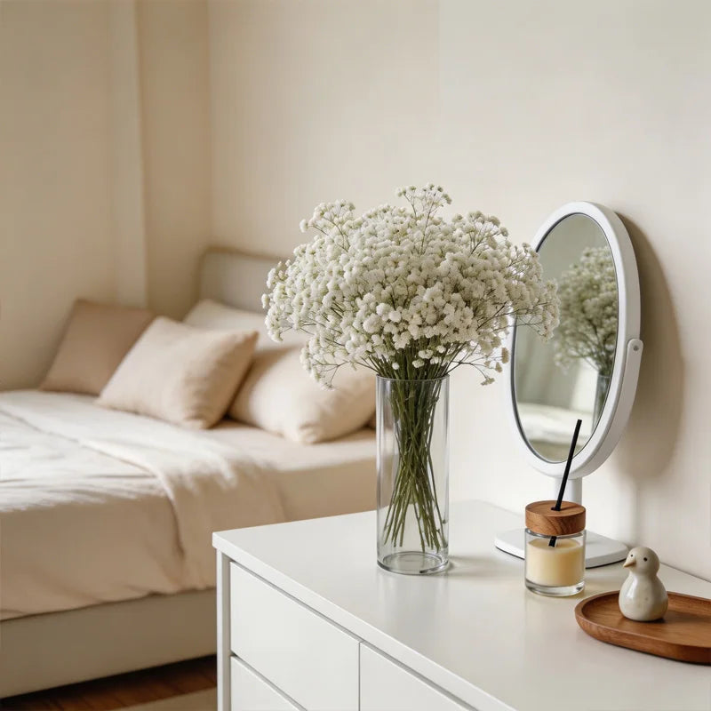 Clear cylinder vase with white baby's breath flowers on a white dresser