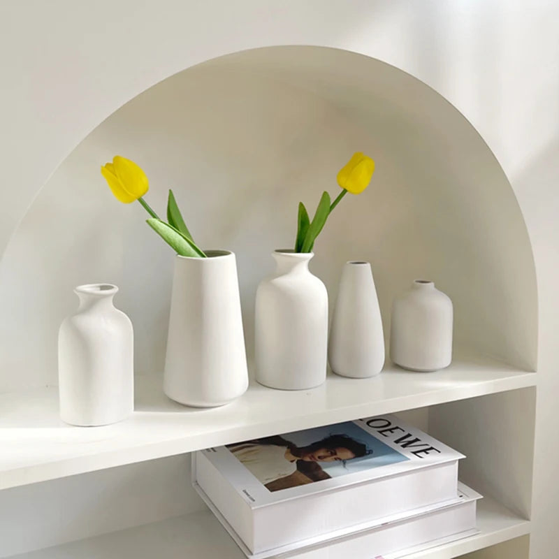 White ceramic vases with yellow tulips on a shelf with books