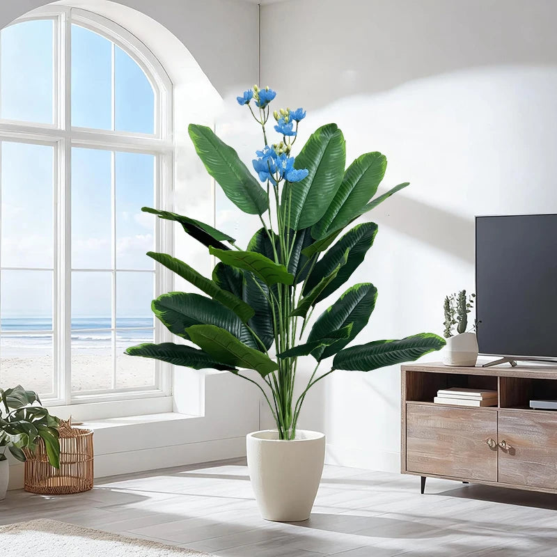 Artificial plant Albína with broad green leaves and blue blossoms in a bright living room