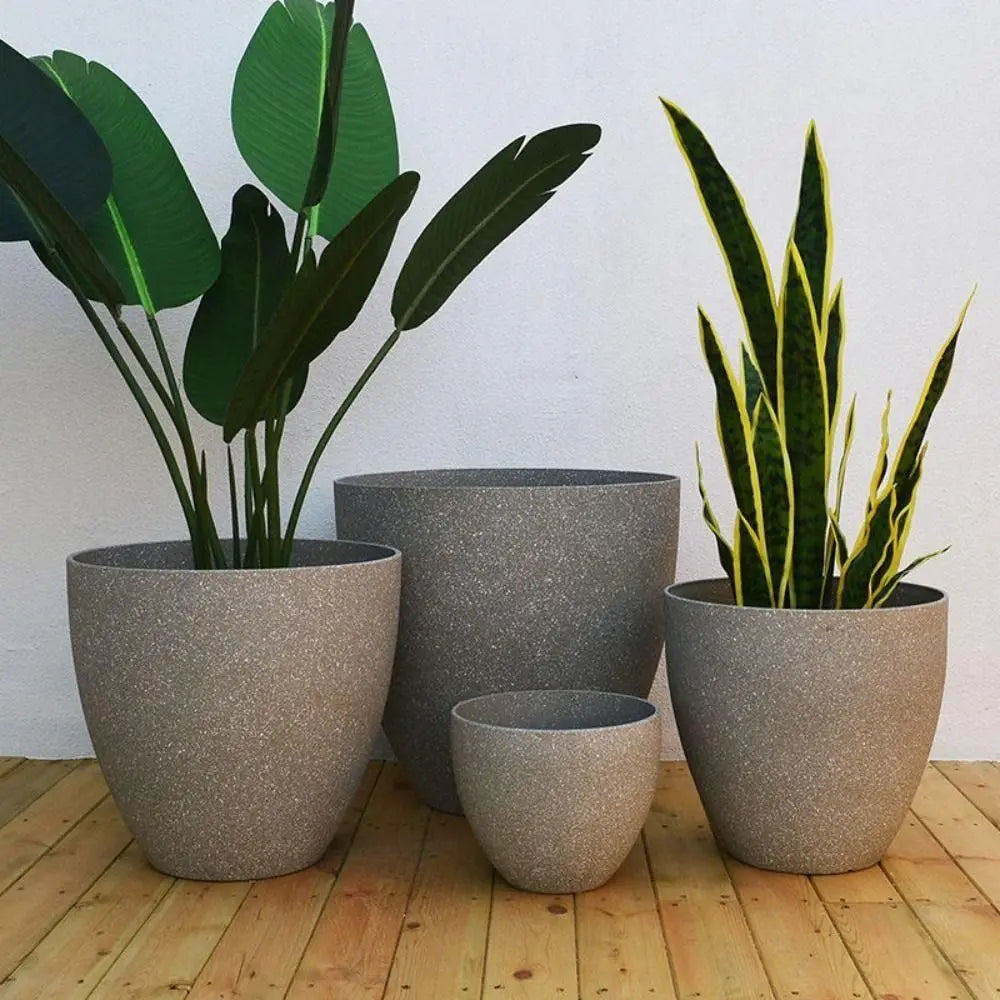 Stone-look planters Ignác in taupe with tall green plants on a wooden floor