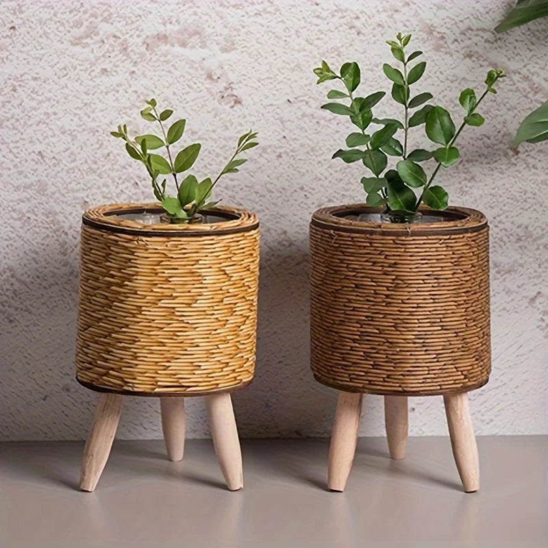 Two rattan planters on wooden legs, light and dark brown cylinders, with small green plants