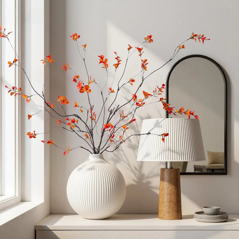 Autumn branches in a ribbed white vase beside a lamp