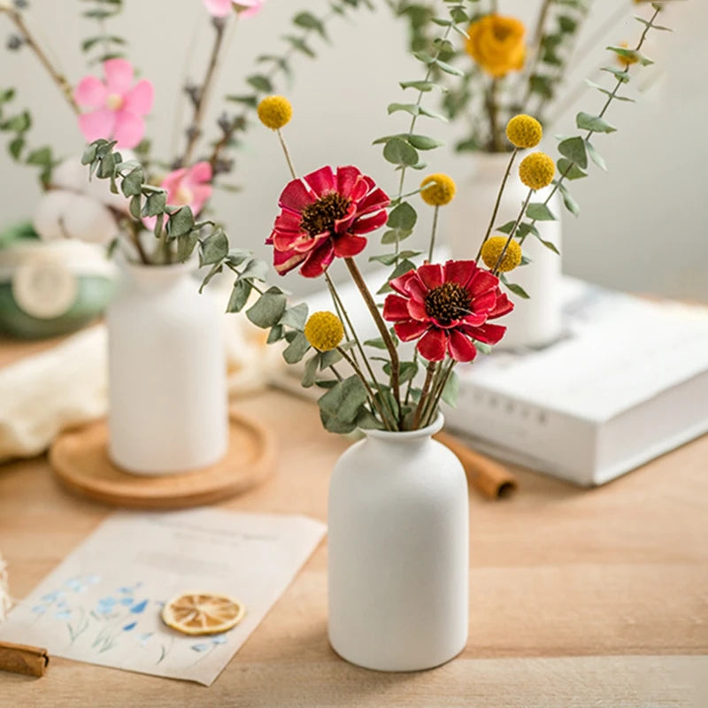 Small white ceramic vase with red and pink dried flowers on a desk