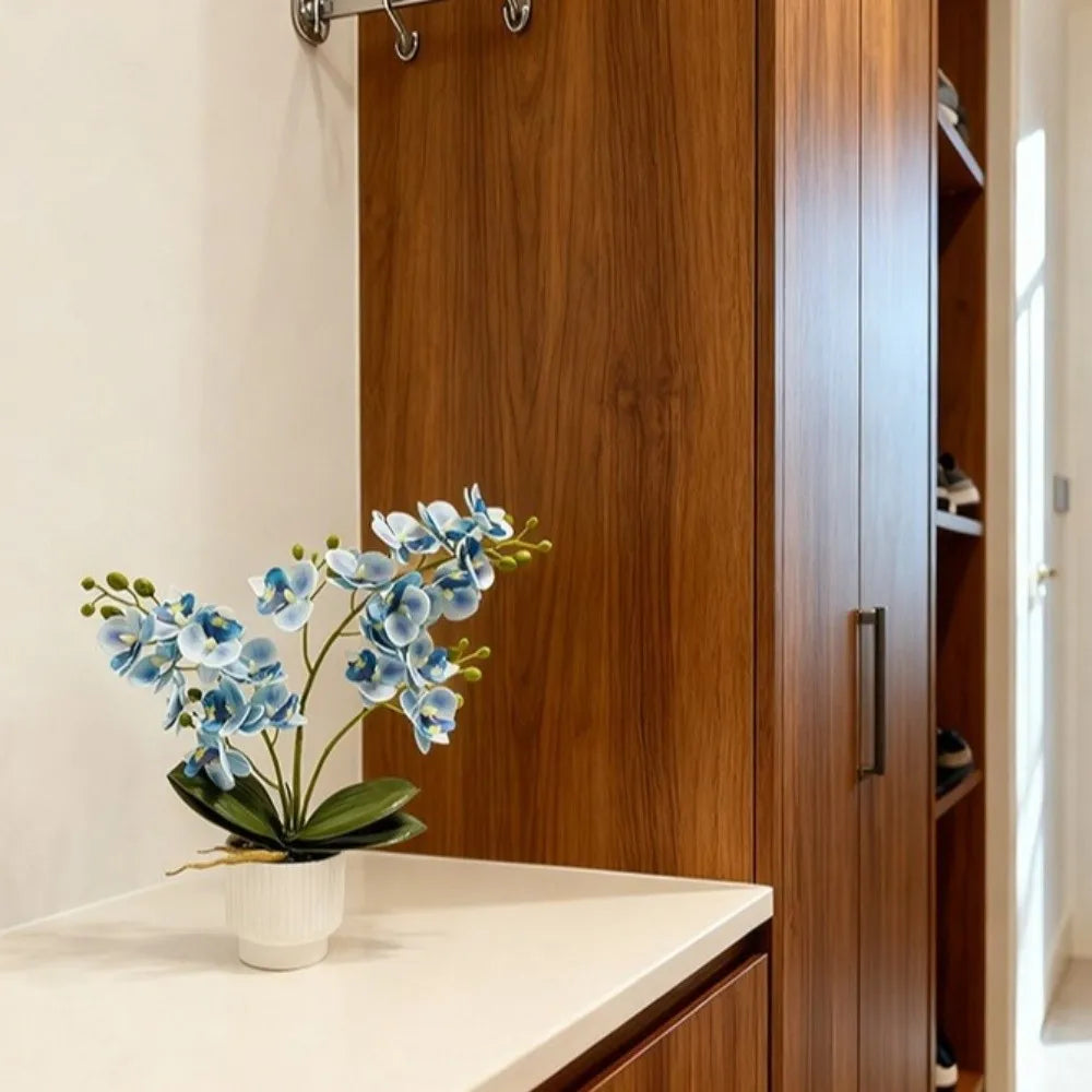 Artificial blue butterfly orchid in a white pot beside a wooden wardrobe