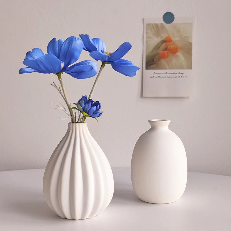 Ridged white ceramic vase with blue flowers next to a round white vase
