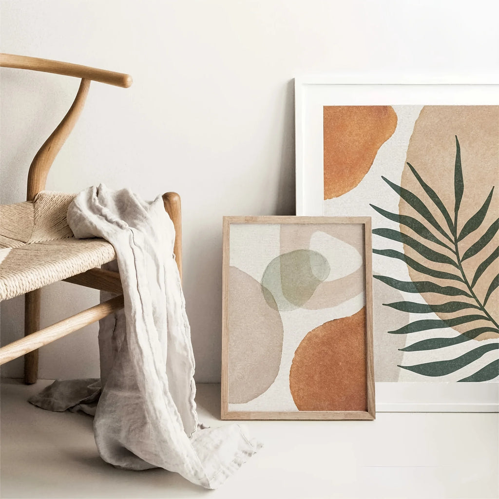Leaf and terracotta art print leaning on the floor next to a chair, shown framed for illustration