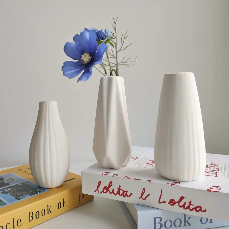 Three matte white ceramic vases in ridged and faceted shapes with a blue flower