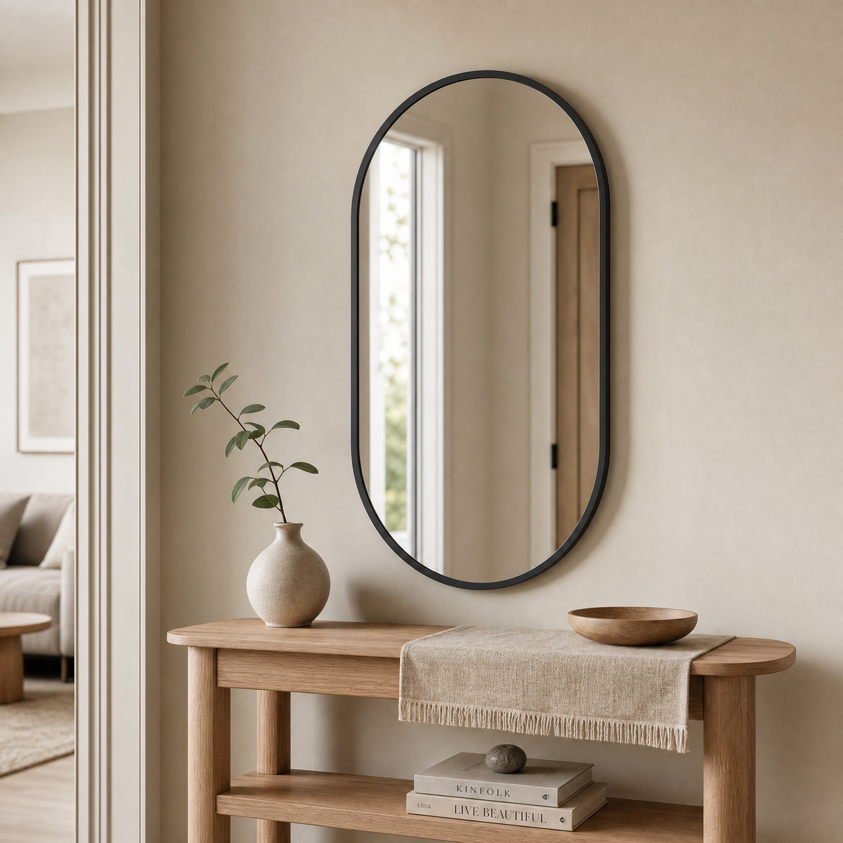 Wall Mirror Simona — slim oval mirror in matte black frame, styled in a warm entryway