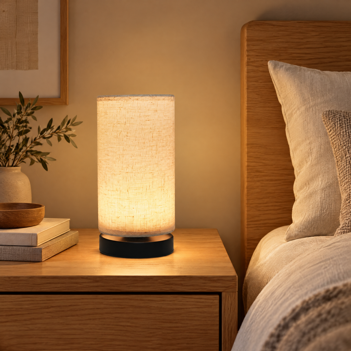 Table Lamp Rastislav on a warm wood nightstand beside a bed, linen shade glowing