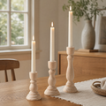 Three graduated unfinished beechwood candlesticks with lit taper candles styled on a warm oak dining table with a linen runner